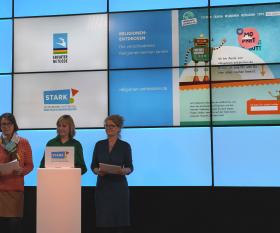 Präsentation der gesiegelten Seiten Screencast einer Kinderseite auf der Leinwand, davor drei Frauen am Pult