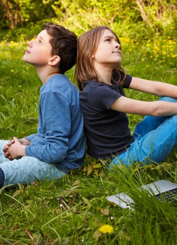 2 Jungen sitzen Rücken an Rücken im Gras und überlegen